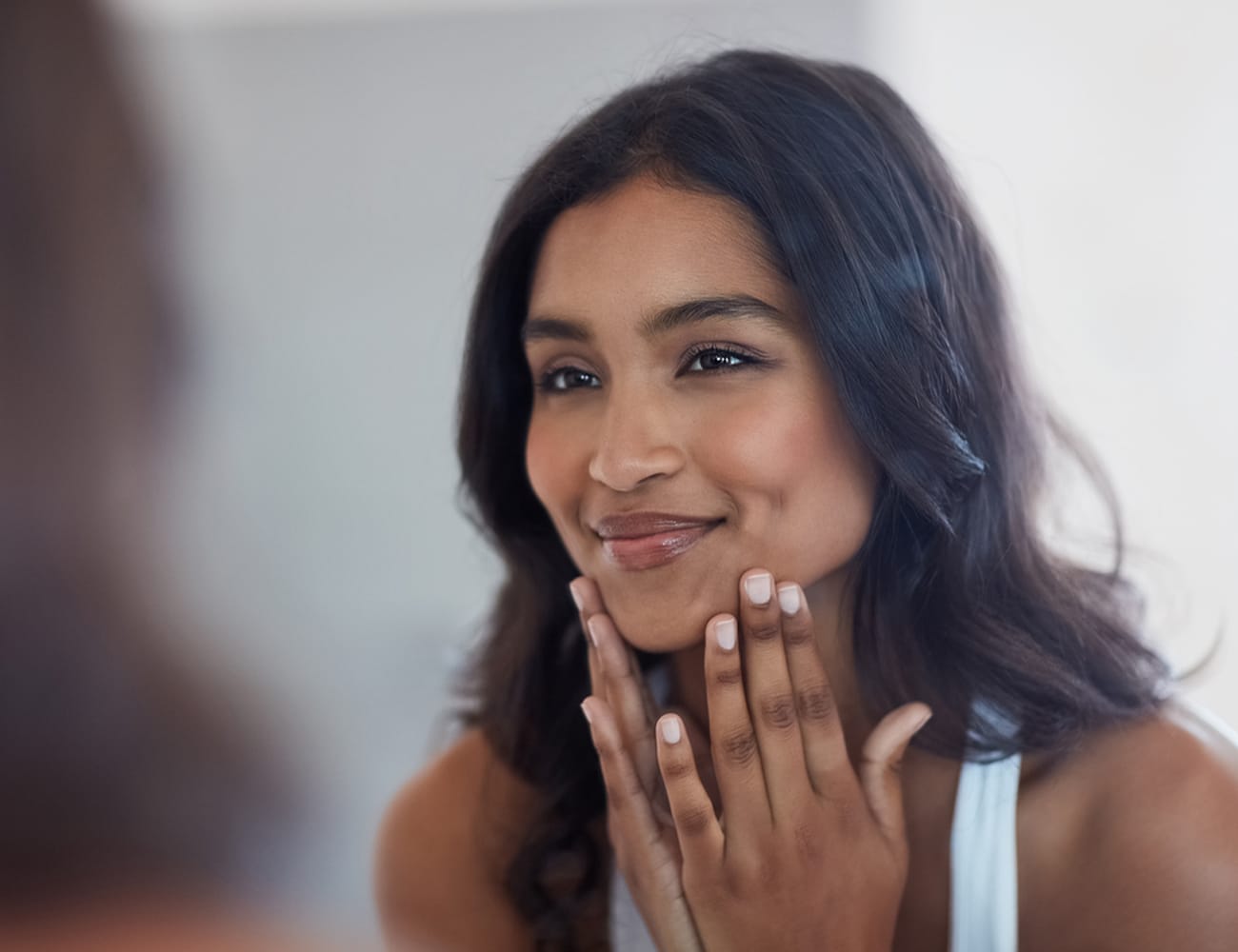 a woman touching her face while looking in mirror